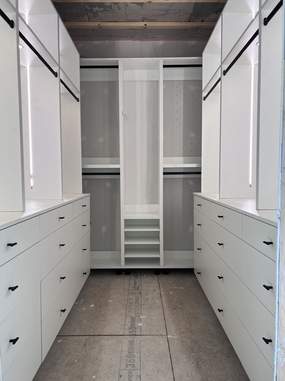 White walk-in closet with black hardware, drawer banks and LED lighting