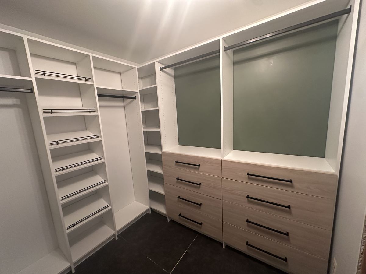 Walk-in closet with white shelving, light wood drawer fronts and soft green accent walls